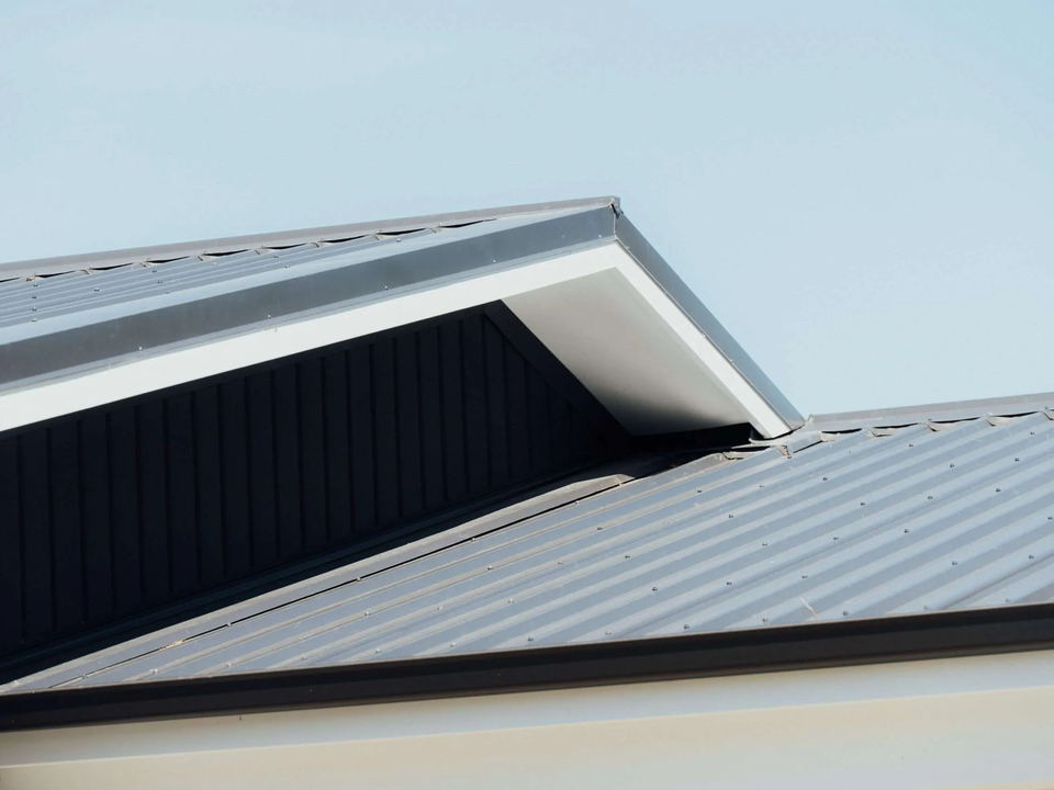 Two levels of dark metal roof meeting neatly, with crisp flashings and white fascia