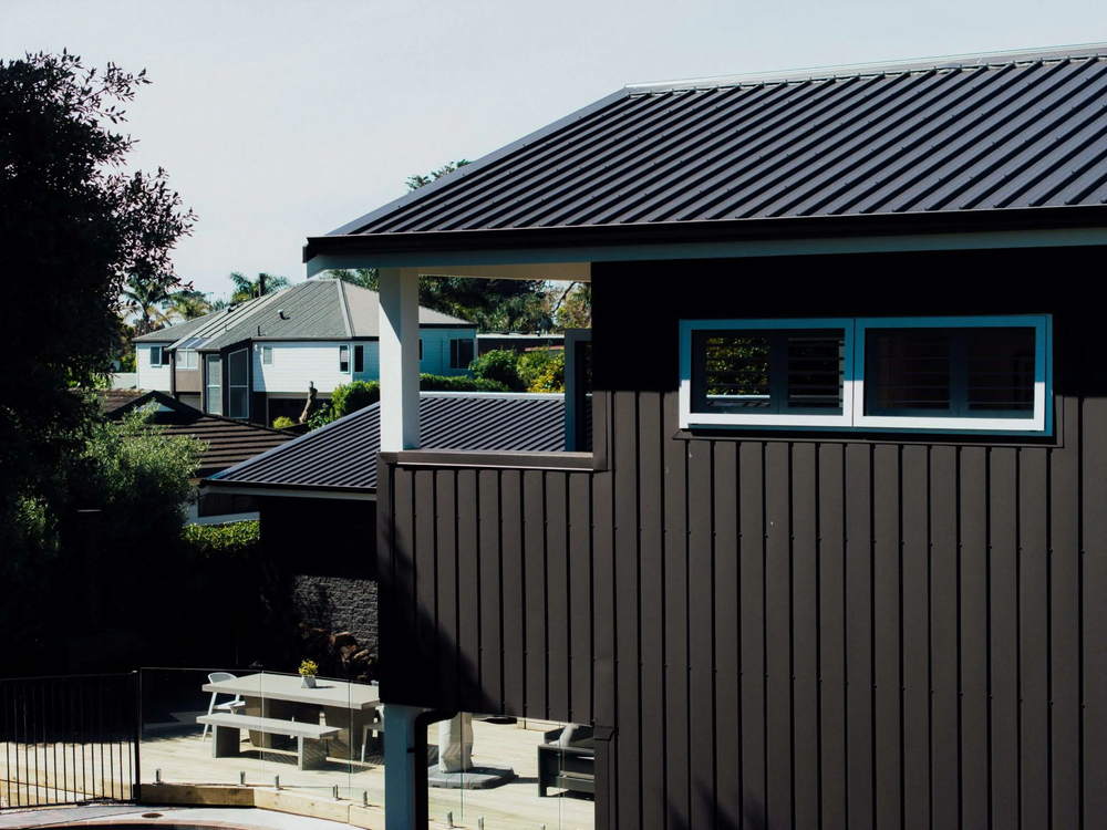 Black vertical cladding and a dark roof on a Tauranga home, with an outdoor table under the eaves