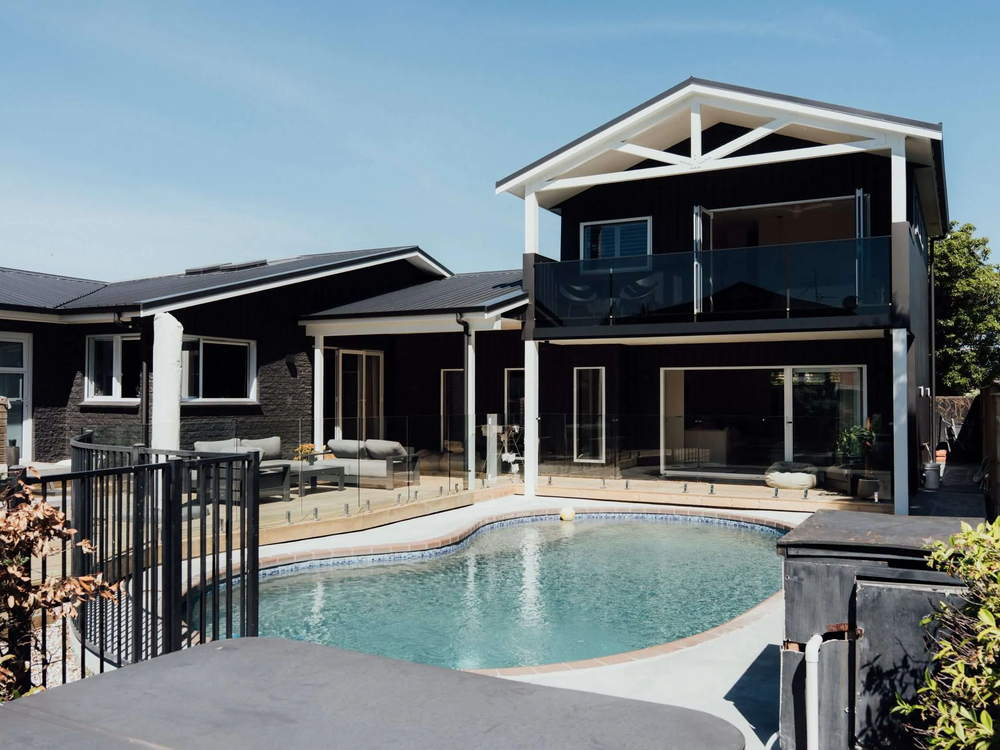 Two storey Tauranga home with a dark roof and glass balustrade overlooking a swimming pool