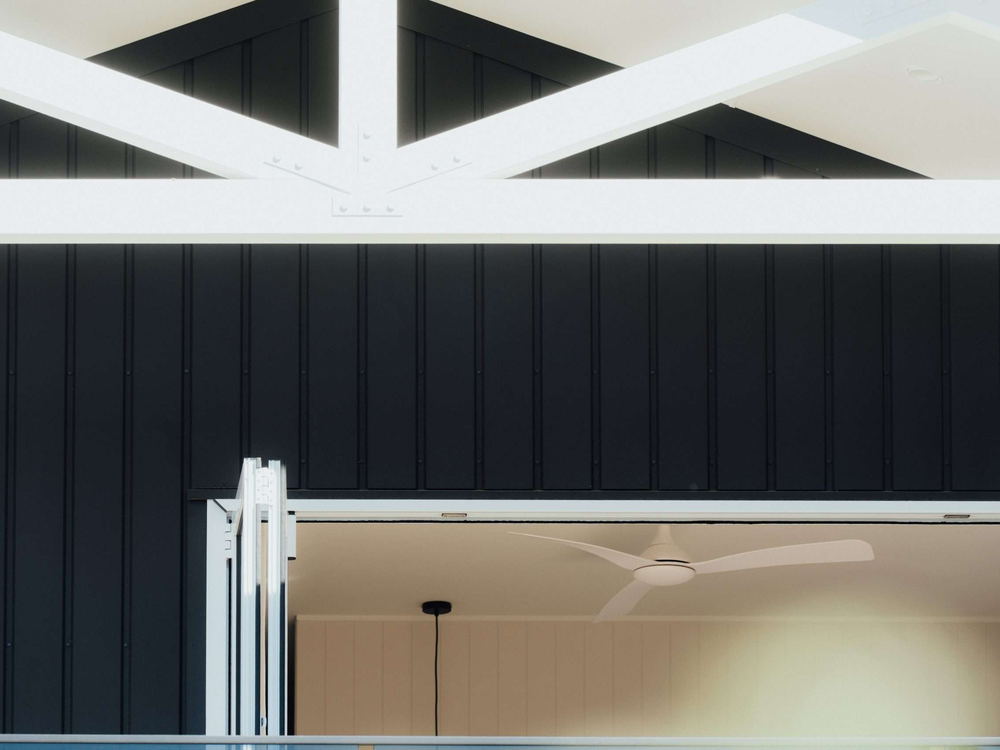 Exposed white timber trusses under a black clad gable, seen from the terrace