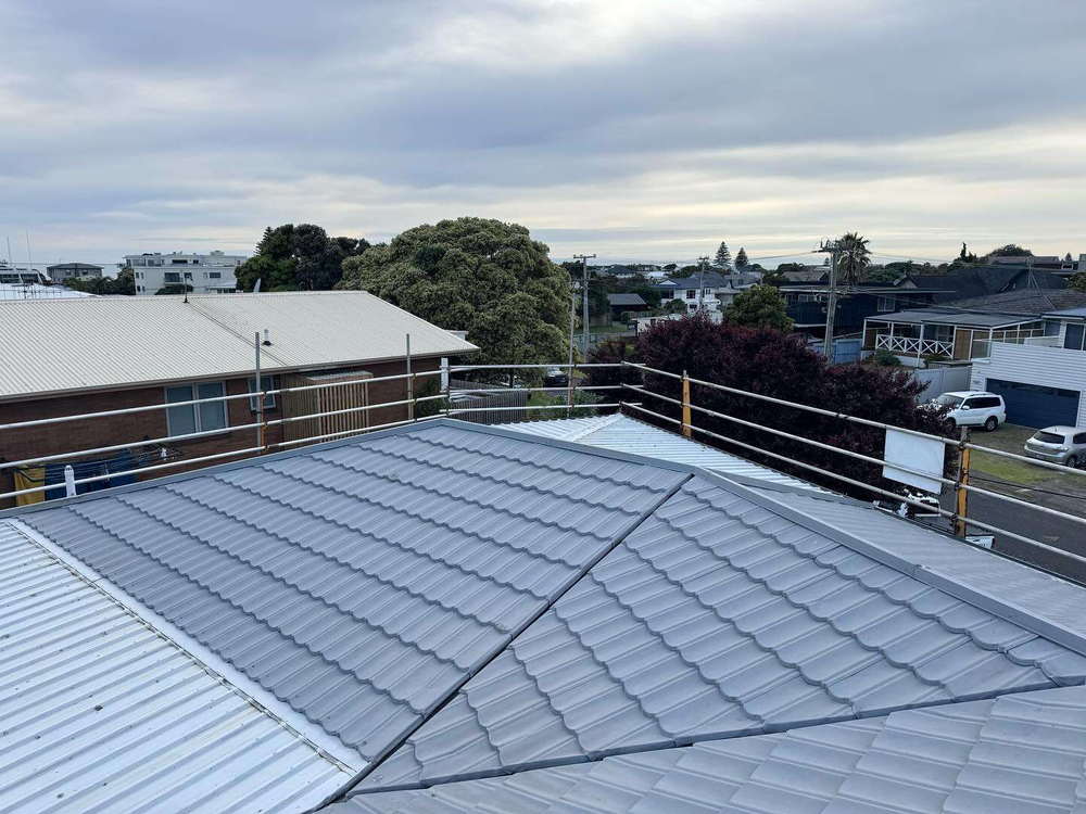 Grey pressed metal tile roof on a suburban house with the town and hills behind it