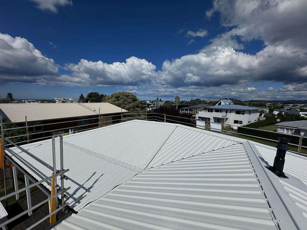 Pale new roofing sheets going down over a Tauranga house with the scaffold rail in the foreground