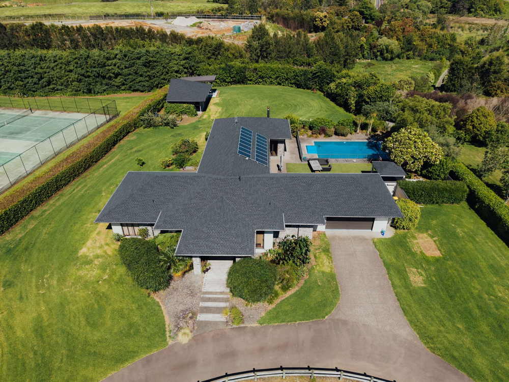 Aerial view of a large lifestyle property with a grey asphalt shingle roof, pool and tennis court
