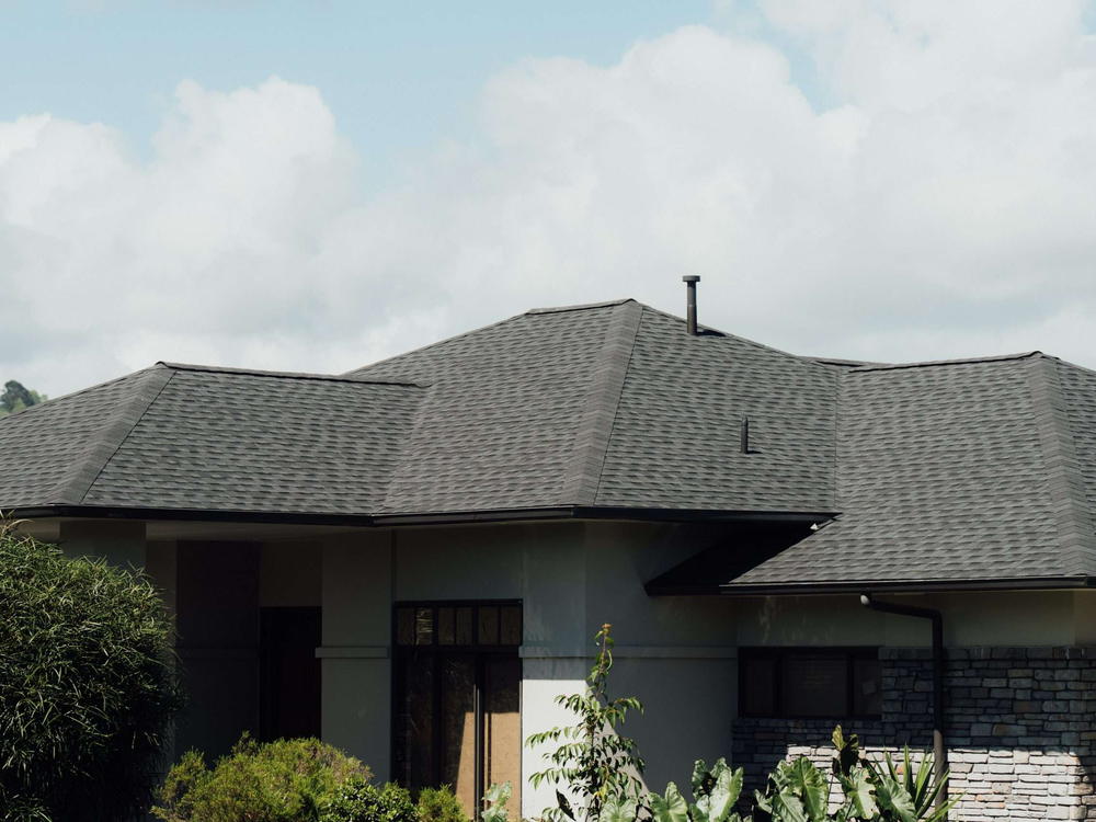 Front of a plastered home with a grey asphalt shingle hip roof and a stone entry