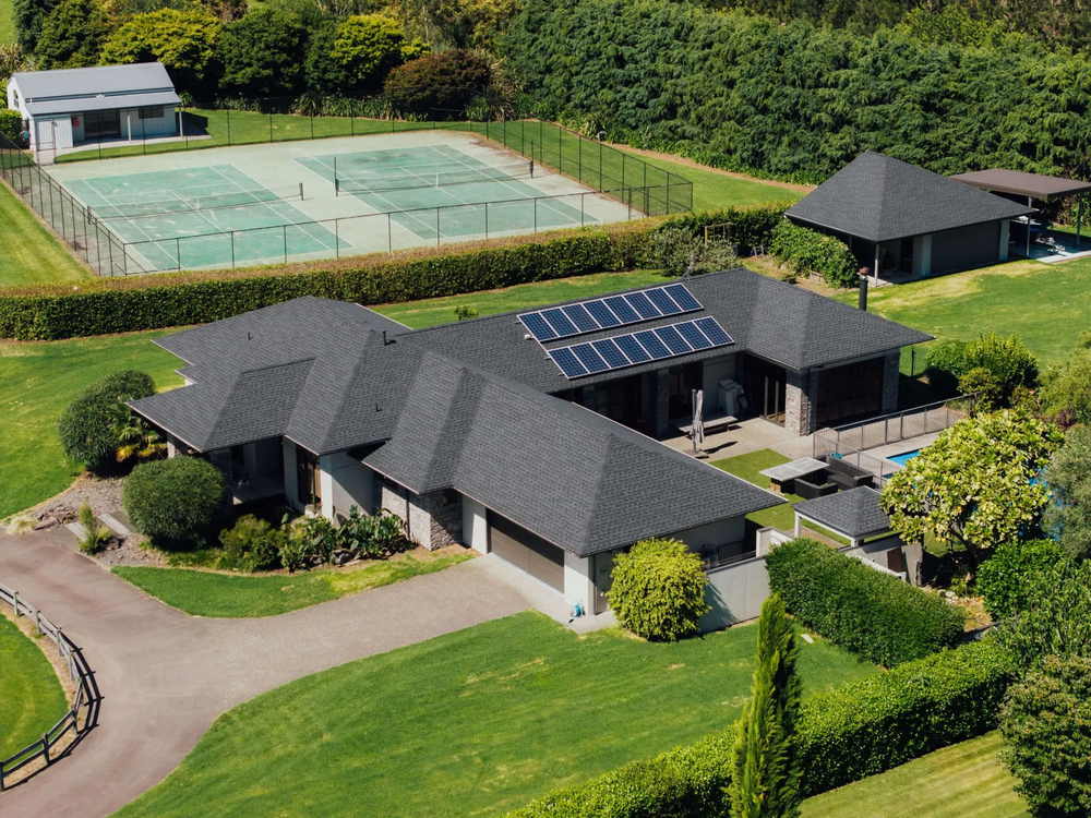 Grey asphalt shingle roof on a lifestyle home with a tennis court and mature hedging behind