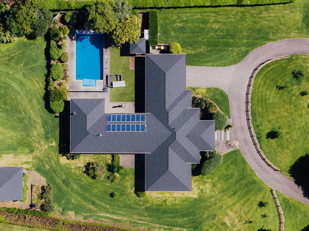 Overhead view of a grey shingle roof with solar panels, a lap pool and a circular drive