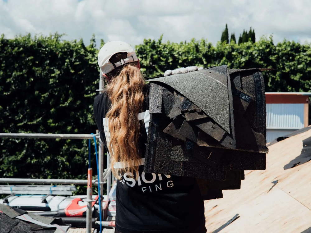 Roofer carrying a bundle of asphalt shingles up onto the roof over one shoulder