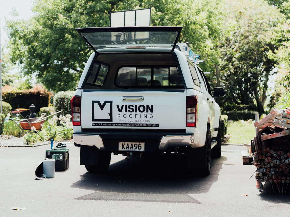 Branded roofing ute parked in a driveway with the canopy open and materials stacked beside it