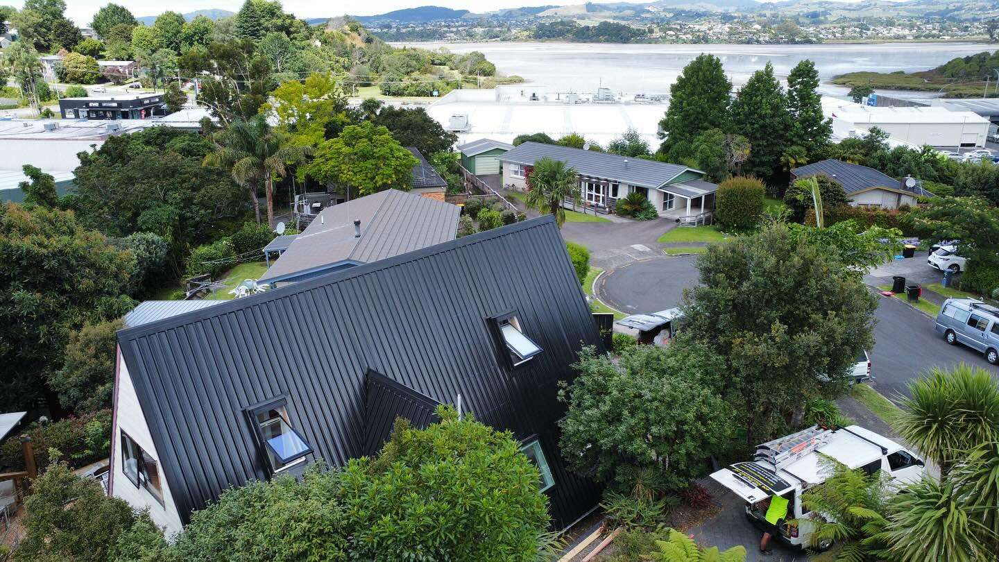Aerial view of a dark roofed house among trees with the Tauranga harbour in the distance