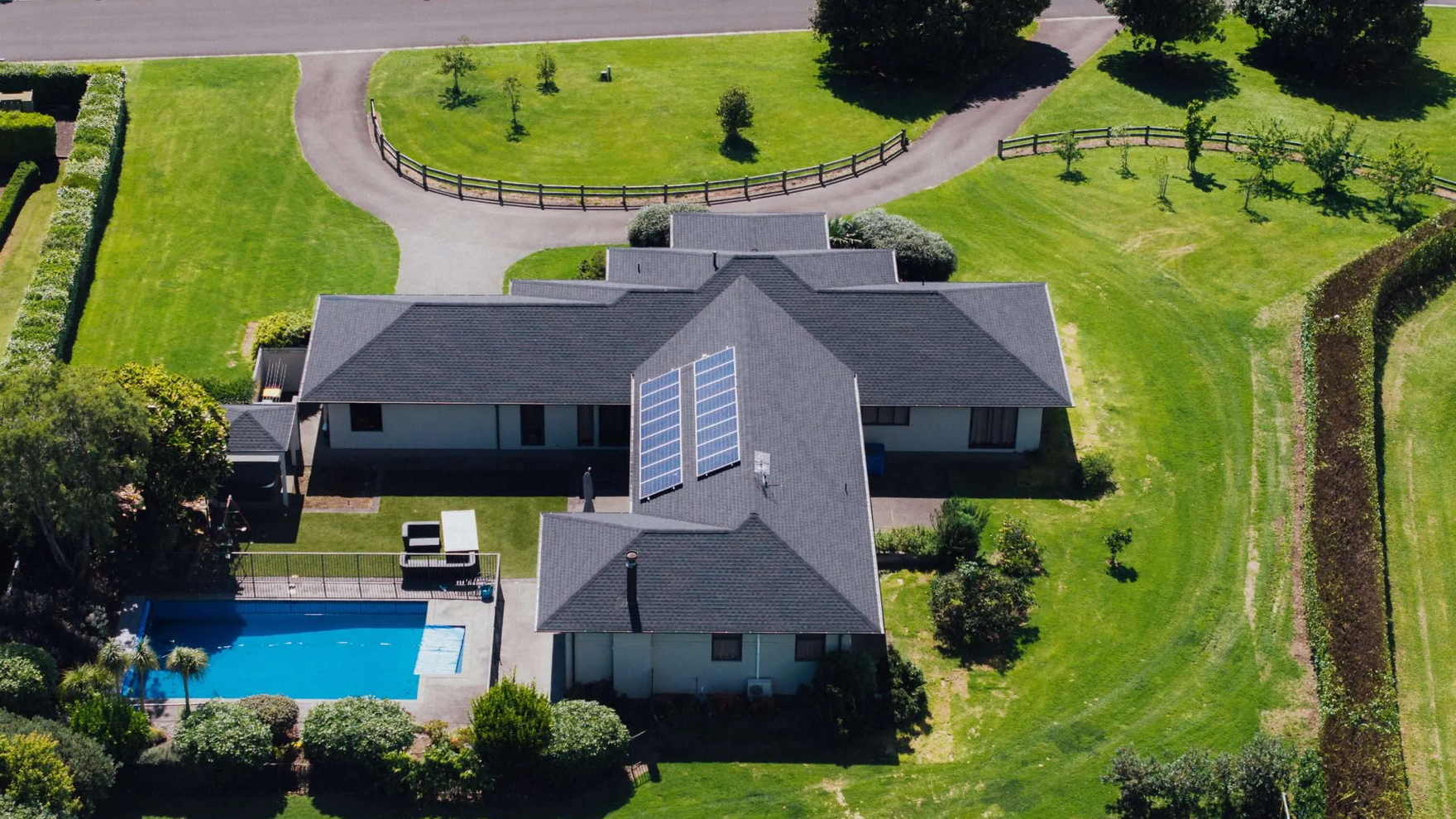 Aerial view of a Tauranga lifestyle property with a grey asphalt shingle roof, solar panels and a pool