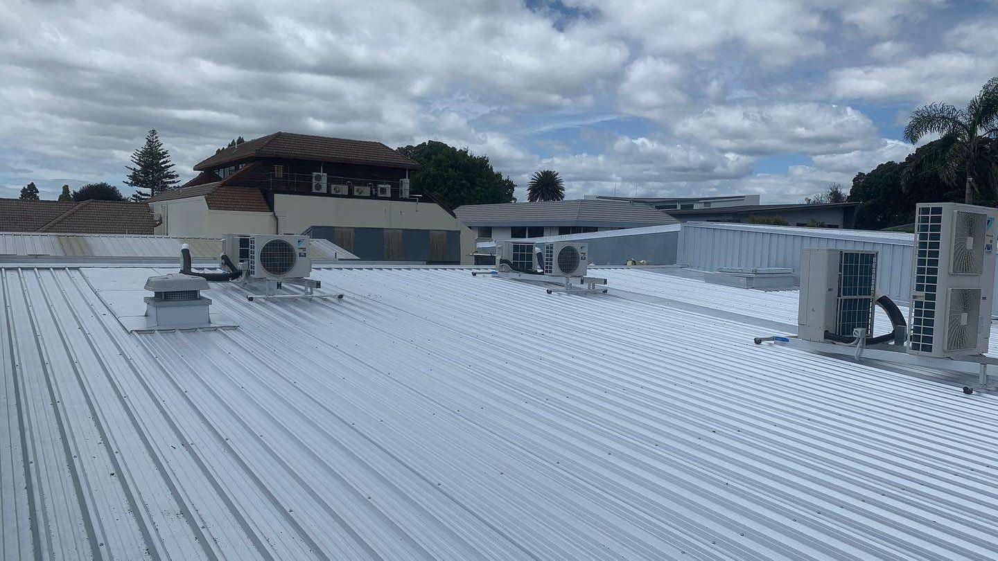 Wide light grey longrun roof over a commercial building with air conditioning units along it