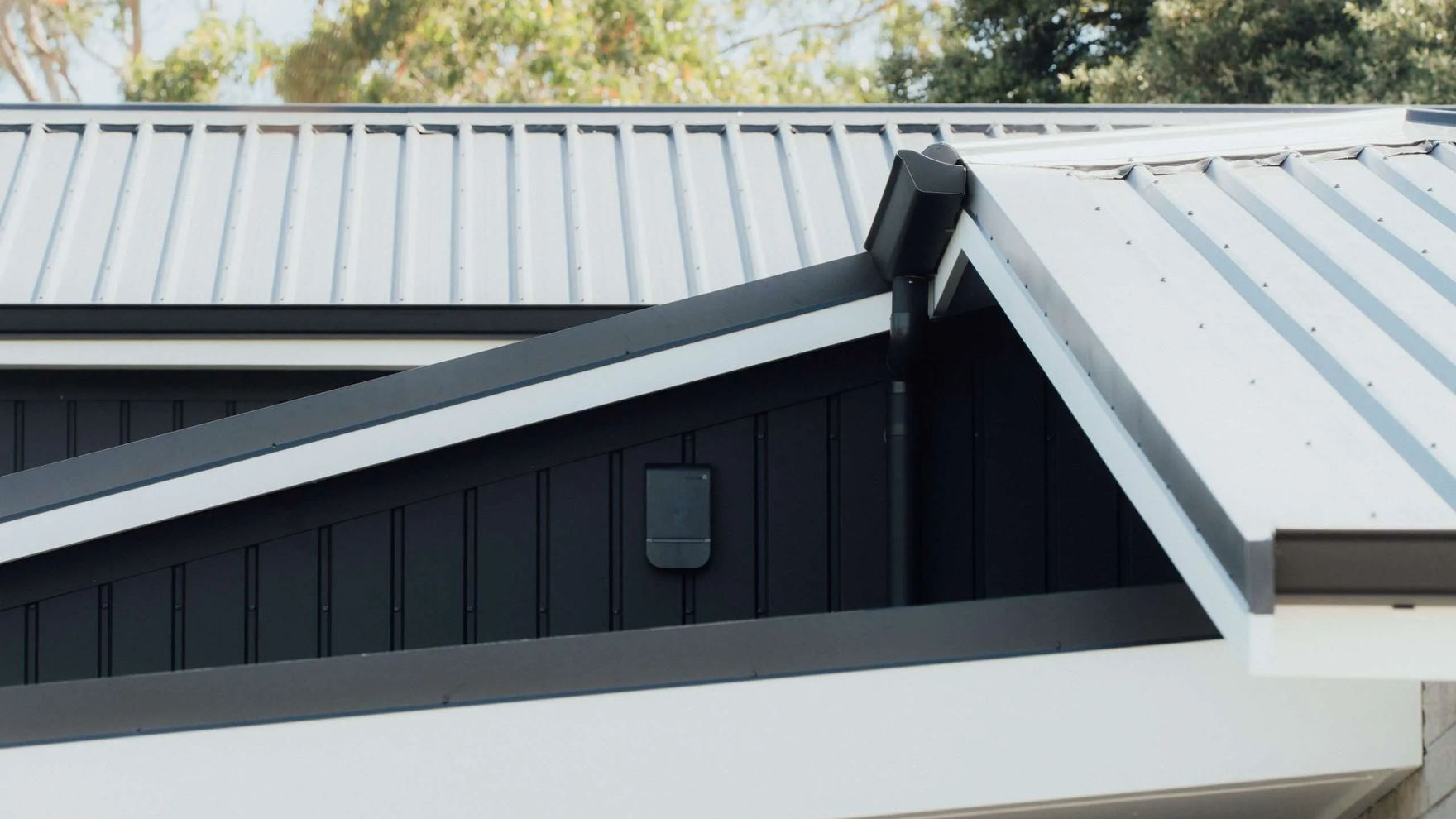 Dark metal roof planes meeting at a ridge on a modern Tauranga home, with white fascia below