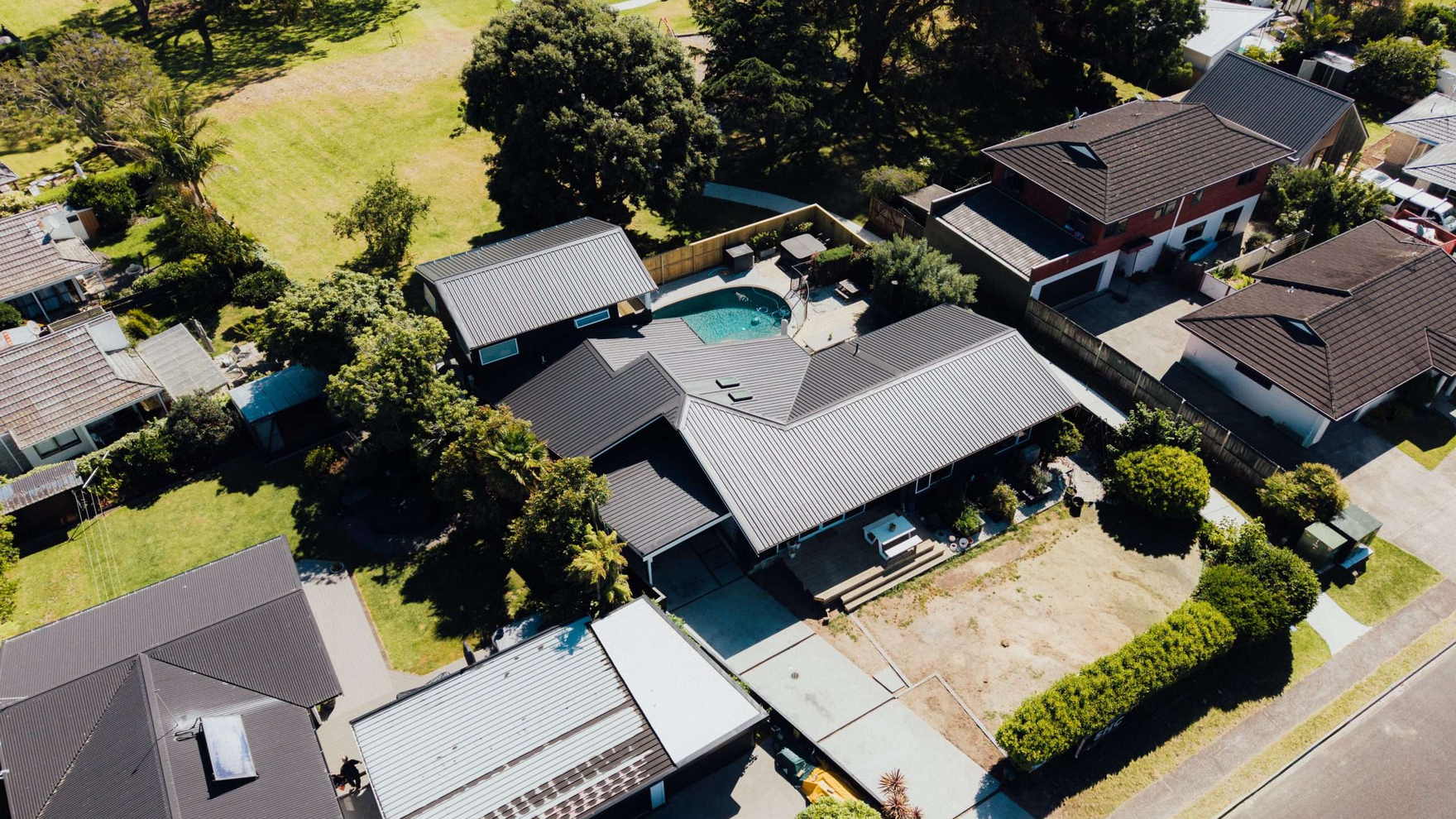 Aerial view over a suburban Tauranga street of a single storey home with a newly installed dark roof