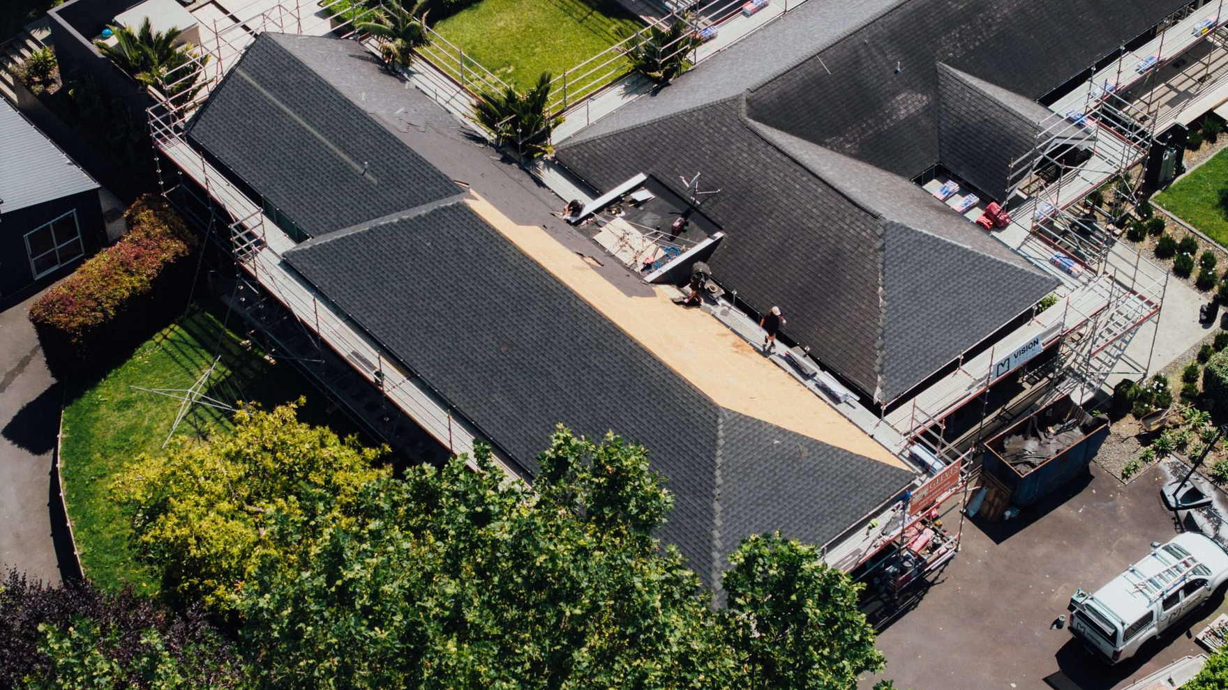 Aerial view of a Te Puna house part way through a re-roof, with the old roof stripped back to bare plywood