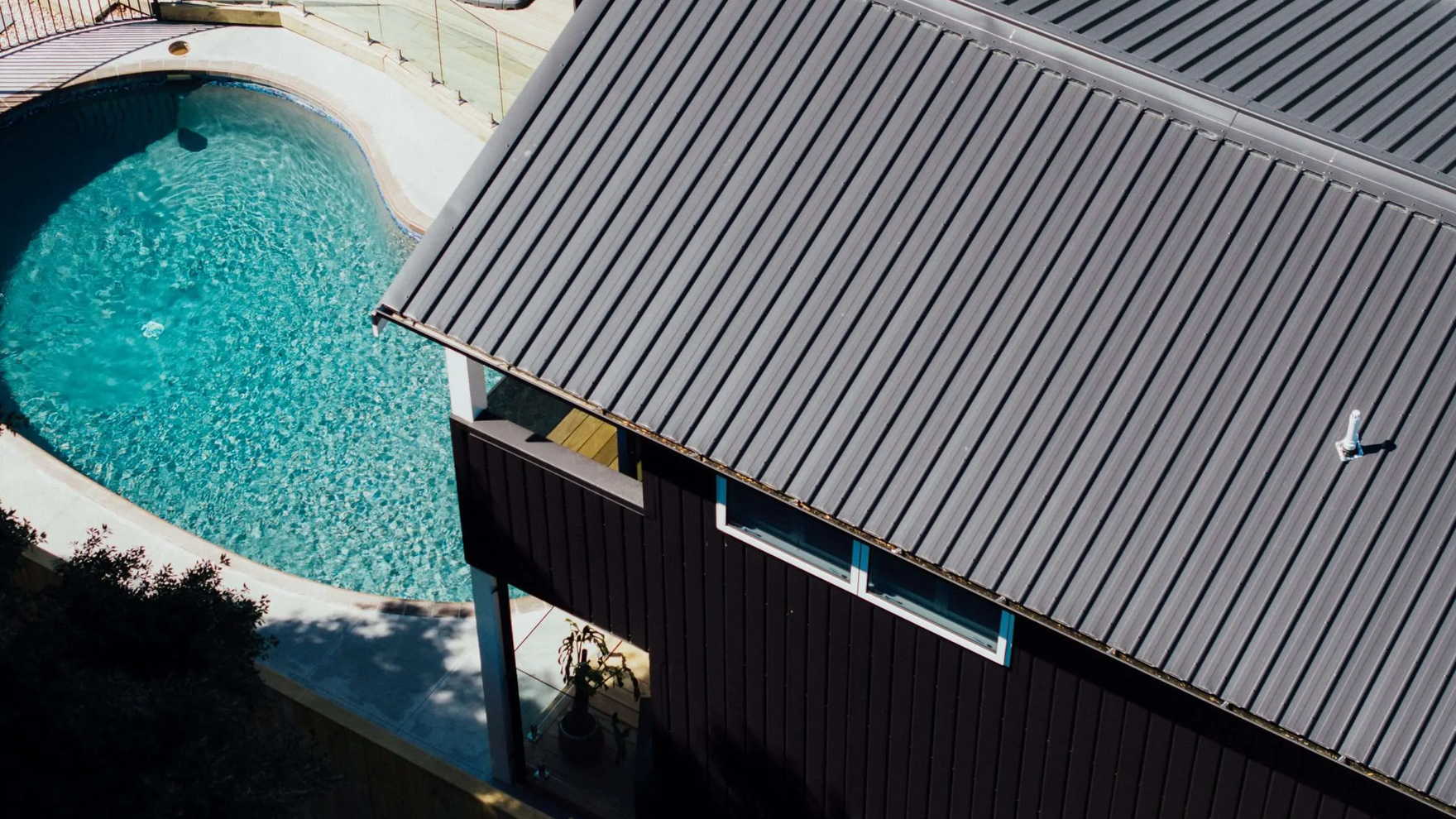 Dark longrun steel roof on a Tauranga home, looking down past the eaves to a turquoise swimming pool