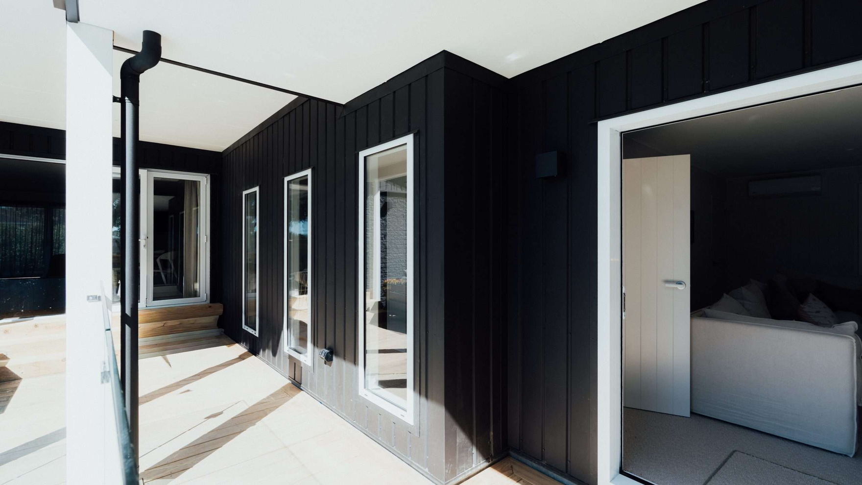 Downpipe running down the corner of a black clad Tauranga home beside a white rendered entry