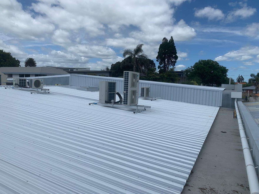 Long light grey commercial roof with heat pump units and a parapet along the edge