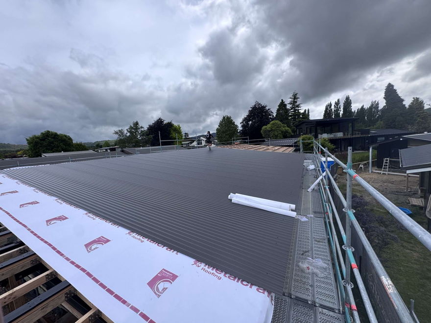 New dark longrun roofing sheets going down over underlay on a Tauranga house