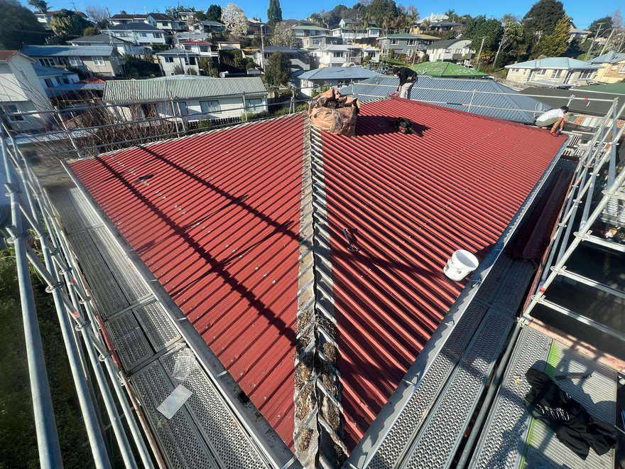 Aerial view of a freshly painted deep red hip roof with a brick chimney